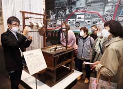 館の職員（左）の「諏訪式繰糸機は、欧米人と比べて体格の小さい日本人女性が1人で作業しやすい構成と配置になっている」などの説明に聞き入る部員