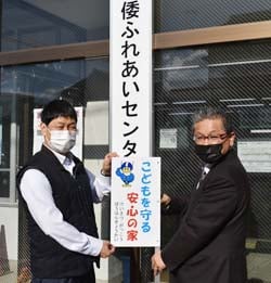 表示板を手渡す青木教頭（左）と福嶋理事（右）