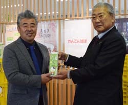 「おもてなし牛乳」を手渡す御子柴組合長（右）