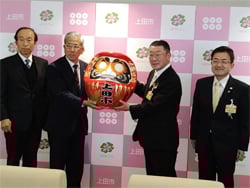 上田市長へだるまを手渡すJA眞島組合長（1月4日、上田市大手）