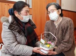 感謝の言葉を添えて利用者に鉢花を手渡す重田代表（左）