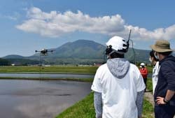 信濃町穂波の圃場でドローンの直播を見守る斉藤社長(写真右)と株式会社グローバルリング社員(写真手前)
