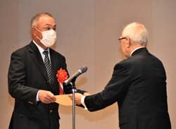 功績を称え表彰状を渡す河崎審査委員長（右）と金賞の佐原さん（左）