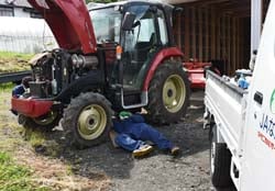 乗用トラクターの下に入り、オイル交換をする職員