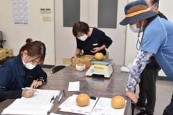 重量の計測を手伝う生産者と結果をまとめるJA職員