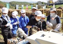 地元組合員（右）の支援のもと、脱穀作業を体験する金沢小学校の児童（長野県茅野市で）