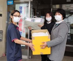 内山さん（左）に清拭布を手渡す部員と職員