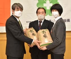 濱野院長（左）に米を手渡す狩戸課長代理（中）と三尾恵技術員（右）