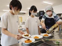 女性部員（右）に教わりながら収録用料理の盛り付けを学ぶ中学生