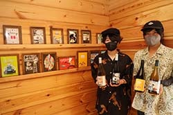 日達さん家族のワインの直売所「ジョルジーニョおじさんの店」に飾られている歴代のラベルを前に、完成したワインを手にする桐子さん（右）と楓子さん（左）