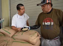 検査員によってトレーに出された米を確認する職員(左)と生産者の佐藤さん(右)
