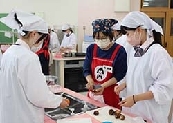 女性部員に指導を受け郷土料理を作る高校生