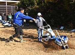 実演会で農業機械を操作する参加者（中央）とメーカー担当者（左）（安曇野市堀金）