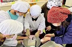 丁寧にボウルに豆腐を移す児童ら