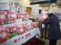 開運だるまをJA職員から受け取る来店者