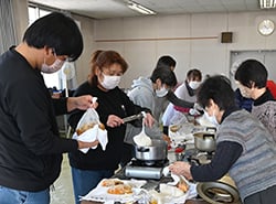 鍋から材料の入ったポリ袋を取り出す参加者(長野県大町市で)