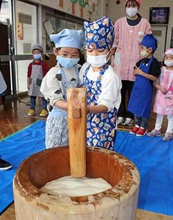 協力し餅つきをする園児