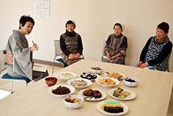 できあがった葬祭料理を前に、横山さん（左）の取材を受ける3人