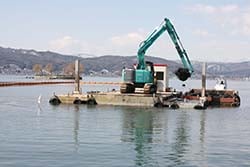 台船に載せた重機で湖底の泥をさらう作業。JA職員ら構成員が見学した