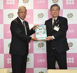 峯村教育長（右）に補助教材を手渡す眞島組合長