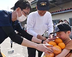 柑橘をサービスするJA職員（左）と組合員家族（右）（安曇野市堀金）