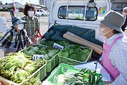 軽ットラ市メンバーと会話を楽しみながら買い物をする買い物客（左)