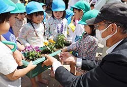 JA役職員（右）からみずべ保育園の園児に花苗のプランターを届けるようす