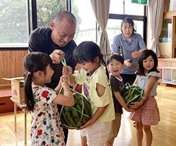 園児にすいかを手渡す粟津原後継営農部長 （左奥) (17日、長野県松本市で）
