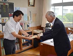 五平餅を手渡す下島専務（右）、受け取る小平学校長