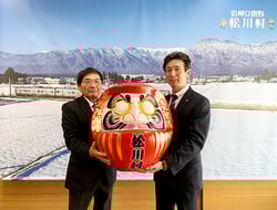 福だるまを手渡す一柳理事（左）と受け取る須沢村長（右）