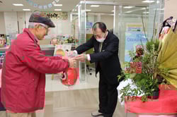 大久保担当理事（右）より福だるまを受け取る来場者（6日、長野県松本市にて）