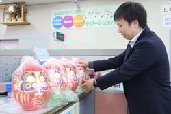 窓口カウンターに進呈するだるまを並べる赤沼主任