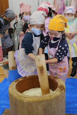 協力し餅つきをする園児