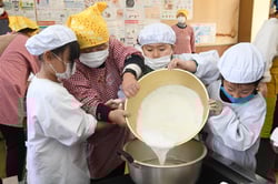 力を合わせて材料を鍋に移す児童と女性部員（長野県長野市、1月28日）