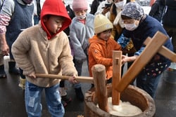 杵を使って餅をつく子供たち