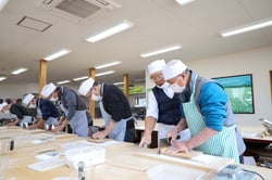 山口さん（右から2人目）のアドバイスのもとそば打ちを行う受講生