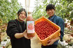 ミニトマトのほ場で「自家製八ヶ岳高原プレミアム　特濃トマトジュース×セロリ」をPRする清水さん（左）と妻の澄枝さん