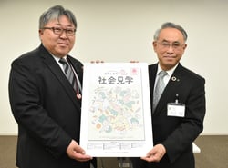 橋渡教育長㊨に冊子のパネル版を手渡す相馬常務