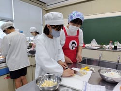 メンバーの指導で慎重に調理する児童