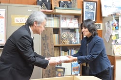 唐澤理事（左）からクレパスを受け取る小林学校長（右）