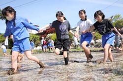 田んぼの中で、土や水と目いっぱいに触れ合う児童（長野県岡谷市で）