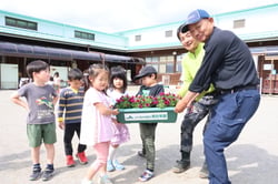 大切に育てたペチュニアのプランターを園児に手渡す野明ブロック長（左）と小島章義副ブロック長