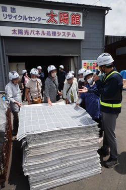 県内初オープンの施設前で太陽光パネルのリサイクルの説明を受ける部員（長野県諏訪市で）