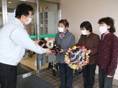 小岩井施設長（左）にリースを手渡す「陽だまりの会」のメンバー