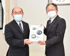 小林政徳校長（右）にファイルを手渡す長岡理事（左）