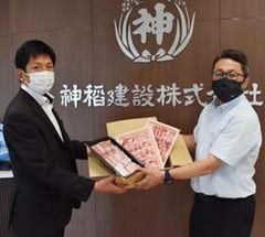 農家支援にとJA内山課長補佐（右）から焼き肉セットを受け取る神稲建設（株）の伊藤部長（左）