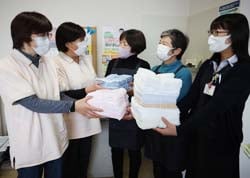 「ケアネットセンターすわこ」の職員に清拭布を手渡す小松幸子ブロック長（中央）と、花岡八重子副ブロック長（右から2番目）、湖北ブロック事務局の志村緋奈乃担当（右）