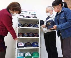 「歴代CAP展」に足を止め、帽子を懐かしむ女性理事と小松八郎組合長
