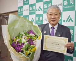 贈られた表彰状と花束を手に笑顔の御子柴組合長