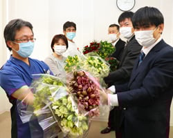 病院職員ら（左側）へアルストロメリアを贈る石崎委員長ら